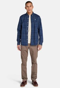 Sininen ruudullinen nappipaita kauluksella, käytetty vaalean paidan päällä. Yhdistetty beigen värisiin chinoihin ja ruskeisiin nauhakenkiin.