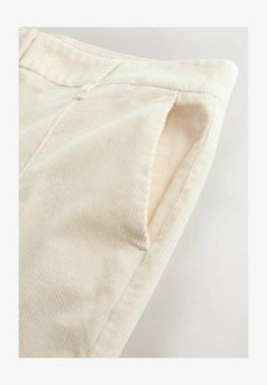 Svetlo béžové nohavice z kordu majú vertikálnu rebrovú textúru, detail postranných vreciek a čisté ukončenie pásu.