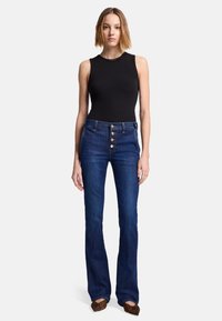 Top senza maniche a righe nere, jeans a zampa d'elefante blu scuro a vita alta con chiusura a cinque bottoni e ballerine con stampa leopardata.