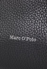 Cuir noir à texture granuleuse avec une surface texturée et un logo blanc en relief, "Marc O'Polo", positionné de manière proéminente à l'extérieur.