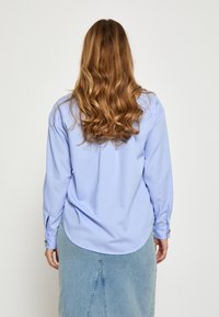 Svetlomodrá košeľa s dlhými rukávmi, zaobleným lemom a gombíkmi na manžetách, skombinovaná so svetlými džínovými sukňami.