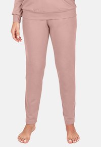 Világos rózsaszín, testre szabott otthoni nadrág sima textúrával és rugalmas derékpánttal, a bokánál szűkülő szabással, egyszerű dizájnt mutatva.