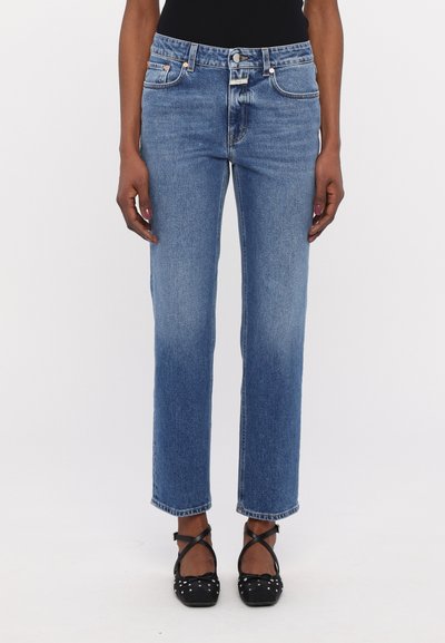 Blue denim straight-leg jeans with a mid-rise waist, five pockets, and subtle fading. Worn with black strappy ballet flats.
