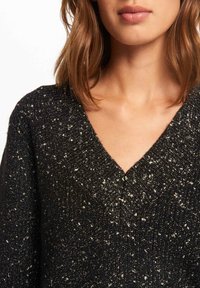 Black V-neck sweater with a textured knit, featuring silver flecks throughout. Soft material and loose-fitting design.