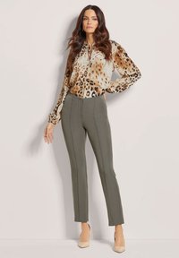 Tijgerprint blouse met lange mouwen en een striknek, gecombineerd met fitted olijfgroene broeken met voornaad en neutrale hakken.