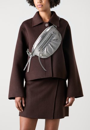 Veste courte en laine marron avec un col, assortie d'une jupe. Sac bandoulière en argent avec zips et clous.