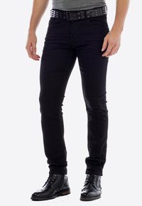 Zwarte skinny jeans met riemlussen, voorzien van een gestikte zwarte riem. De jeans hebben een lichte glans en zijn gestyled met zwarte veterschoenen.
