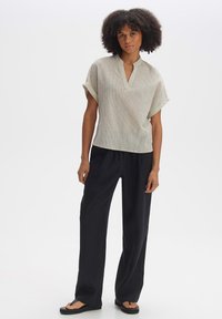 Top grigio chiaro a maniche corte con scollatura a V e sottili righe verticali, abbinato a pantaloni neri a gamba larga e sandali flat.