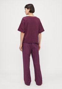 T-shirt en coton violet oversized avec des manches amples, associé à un pantalon large assorti, tous deux présentant une texture lisse et une coupe décontractée.