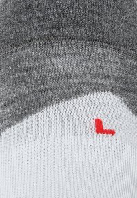 Szare i białe skarpetki z teksturowanym wzorem dzianiny, z wyraźnym czerwonym symbolem "L" w pobliżu kostki.