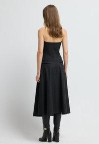 Czarny top bez ramiączek w zestawie z rozkloszowaną czarną spódnicą, wykonaną z teksturowanej tkaniny. Modelka nosi czarne kozaki za kolano z złotymi akcentami.