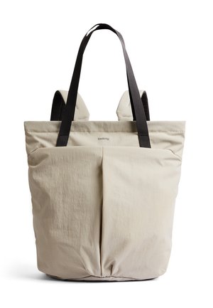 Borsa a mano beige con spallacci neri e spallacci imbottiti da zaino, caratterizzata da una cucitura verticale frontale e un logo del marchio discreto al centro in alto.