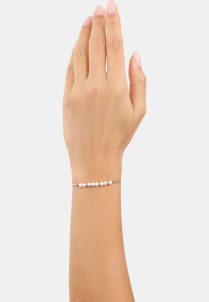 Pulsera de plata con una fila de pequeñas perlas blancas, reposando sobre una mano de tono de piel neutro contra un fondo blanco liso.