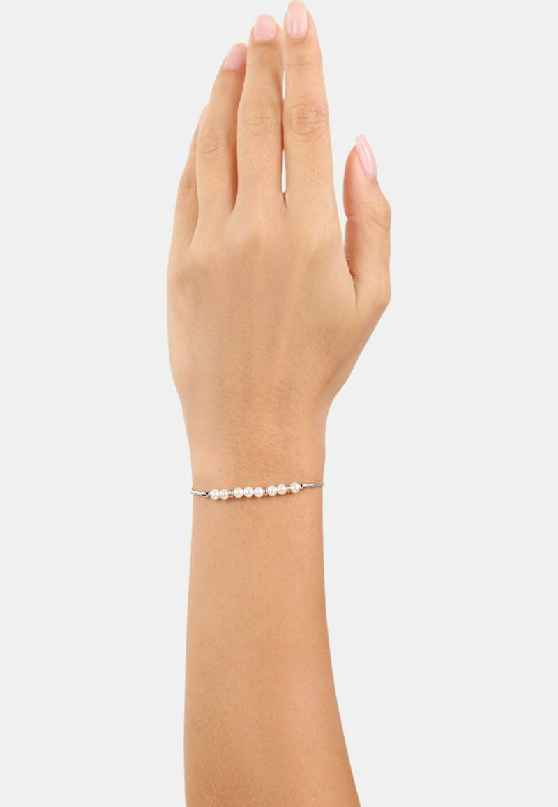 Bracciale d'argento con una fila di piccole perle bianche, poggiato su una mano con un tono di pelle neutro su uno sfondo bianco semplice.