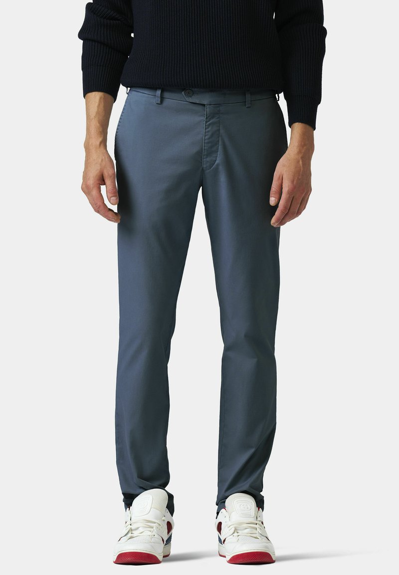 Graue Baumwollhosen mit schlanker Passform. Sie haben einen flachen Bund, Gürtelschlaufen und seitliche Taschen. Kombiniert mit weißen Sneakern mit roten Akzenten.