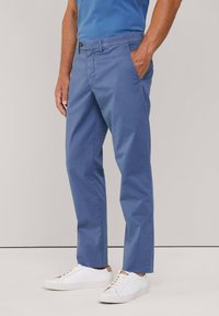 Pantalones de color azul claro hechos de algodón, con corte recto, bolsillos frontales y cierre de botón. Combinados con zapatillas blancas.