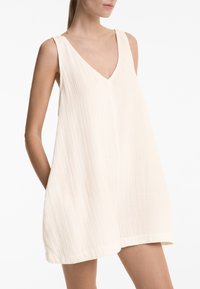 Lässiges ärmelloses Kleid in Off-White, mit V-Ausschnitt und strukturiertem Stoff, seitlichen Taschen und geradem Saum.