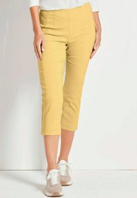 Geel capri-broeken met een zachte textuur en een taillering, voorzien van voornaaien en een knielang zoom, gecombineerd met lichtgekleurde sneakers.