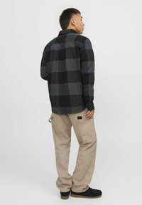 Zwart en grijs geruite flanellen shirt met lange mouwen, gecombineerd met beige cargobroeken met meerdere zakken en een gestructureerd oppervlak.