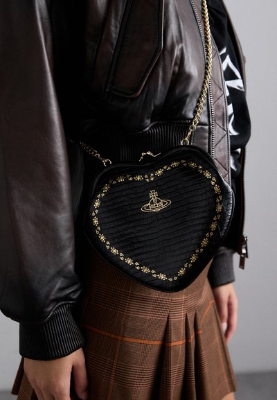 Zwarte hartvormige tas met een textuurdesign, gouden bloemenaccenten en een kettingband, gedragen met een bruin geruite rok en een leren jasje.