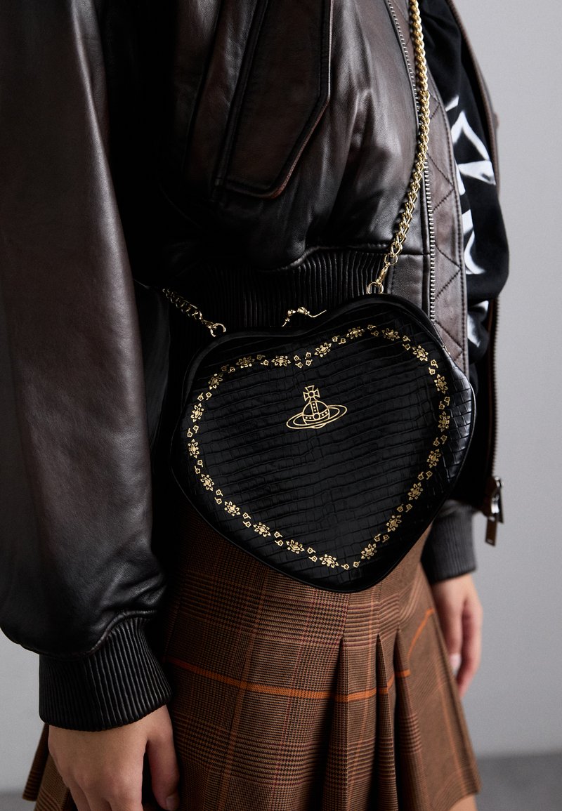 Μαύρη τσάντα σε σχήμα καρδιάς με υφή, χρυσές ανθισμένες λεπτομέρειες και αλυσίδα, συνδυασμένη με καφέ καρό φούστα και δερμάτινοJack.