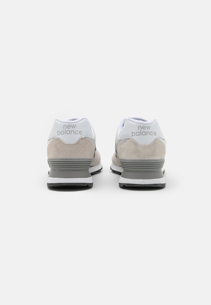 Zapatillas New Balance en gris y blanco con materiales de ante y malla, forma redondeada y suela contrastante. Logo visible en el talón.