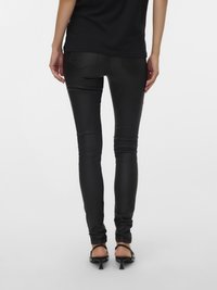 Jean skinny en fausse cuir noir à texture lisse, avec poches arrière et coupe ajustée, associé à des sandales à talons noires.