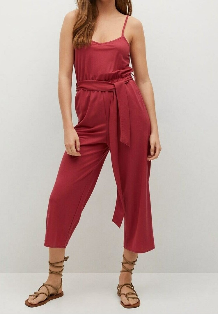 Combinaison bordeaux avec des bretelles spaghetti, taille cintrée et ceinture nouée. Texture lisse, jambes larges courtes, associée à des sandales à lanières.