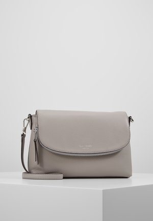 Bolso bandolera de cuero gris claro con cierre de solapa y detalle de cremallera, descansando sobre un pedestal geométrico blanco contra un fondo liso.