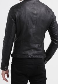 Musta nahkatakki tyylikkäällä muotoilulla, jossa on istuva leikkaus, näkyvät saumat ja sileä pinta. Ei lisäkoristeita.