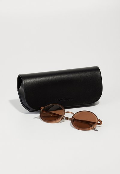 Brown round sunglasses with thick frames and silver accents beside a black leather case, featuring a smooth texture and embossed logo.