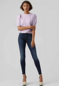 Suéter de punto lila con mangas abullonadas, combinado con jeans ajustados azul oscuro y tacones de plataforma beige. Diseño sencillo con silueta ajustada.