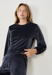 Top lungo in velluto blu navy con texture a coste, scollo rotondo e polsini aderenti, abbinato a pantaloni coordinati con texture.