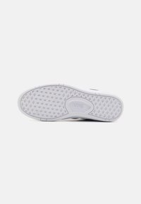 Fehér gumitalpú sportcipő, hexagonális mintával és egy kis "VANS" logóval beágyazva. Lapított forma és sima élek.