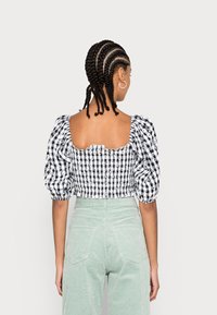 Blusa xadrez em preto e branco com mangas bufantes e decote quadrado, usada com calças de sarja verde menta de cintura alta.