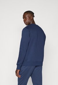 Sudadera azul marino con cuello redondo, puños acanalados y dobladillo. Textura suave y diseño ajustado, mostrada desde la parte de atrás.