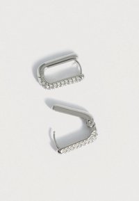 Ασημένια μεταλλικά σκουλαρίκια σε σχήμα κρίκου που διαθέτουν μια σειρά από διαφανείς ρινοστάτες κατά μήκος της εμπρόσθιας άκρης. Ο σχεδιασμός είναι κομψός με κλείσιμο με μεντεσέ.