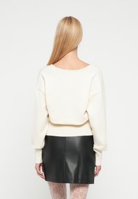 Pull en maille crème oversize avec un large col rond, associé à une mini-jupe en cuir noire. Manches longues avec poignets côtelés.