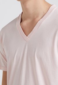 T-shirt rosa chiaro a scollo a V realizzato in tessuto morbido, caratterizzato da una vestibilità rilassata e maniche corte. Leggera texture con dettaglio a contrasto sul collo.