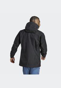 Giacca impermeabile nera con cappuccio. Presenta maniche lunghe, una vestibilità comoda e una texture opaca liscia. Design minimalistico senza loghi visibili.