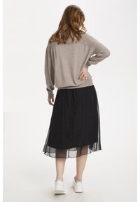 Ljusbrun oversized tröja, svart lager-på-lager kjol med genomskinlig överlagring och vita sneakers. Mjuk textur och avspänd silhuett.