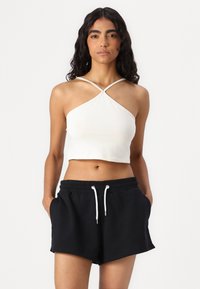 Valge lühike halter-top, millel on ristuvad rihmad ja toored servad, koos mustade lõhikute pükste ja küljetaskutega.