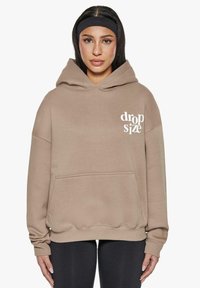 Beige Kapuzenpullover mit einer frontalen Tasche, ausgestattet mit weißem "drop size" Text. Hergestellt aus weichem Material, verfügt er über gerippte Bündchen und einen Saum.