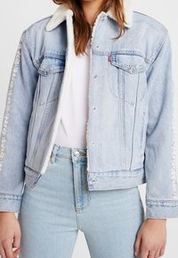Jasnoniebieska kurtka dżinsowa z kołnierzem z baranka, przednimi kieszeniami oraz kwiatowym haftem na rękawach. Standardowy krój i długość.