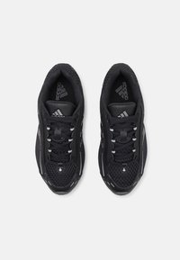 Black athletic shoes with a mesh upper, textured accents, reflective details, and a lace-up design. Logo prominently displayed on the tongue.