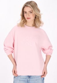 Felpa rosa con stampa testurizzata "SOFT SOUL", taglio rilassato, scollo rotondo e maniche lunghe, abbinata a pantaloni in denim chiaro.