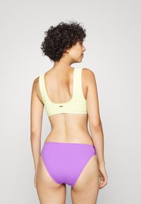 Gulruter bikini topp med brede stropper, kombinert med ensfargede lilla bikinitruser. Glatt tekstur, snug passform og minimal hardware-detalj.