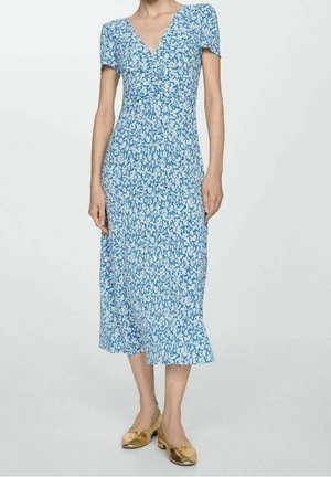 Blauwe midi-jurk met bloemenpatroon, V-hals en korte mouwen, met een aansluitend lijfje en een vloeiende rok. Gouden schoenen maken de outfit compleet.