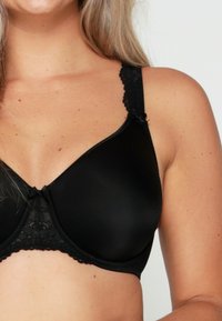 Zwarte bh met gepatte cups, kantdetails langs de band en de bandjes, verstelbare bandjes en een kleine strikaccent in het midden.