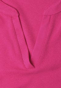 Tissu rose vif avec un décolleté en V profond, col plié et coutures visibles le long des bords.